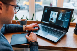 Photographer is processing photo on laptop, sitting at cafe